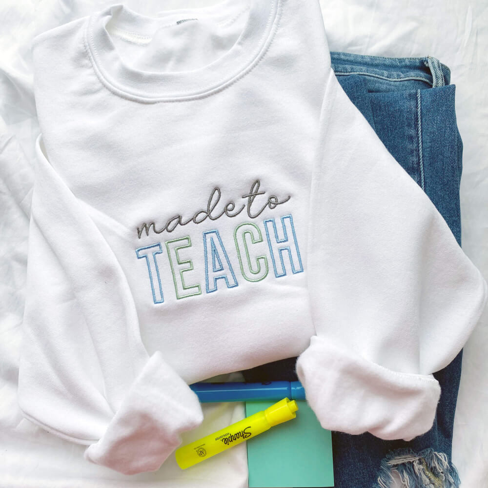 white sweater with blue, green, and gray font spelling the words ‘made to teach’