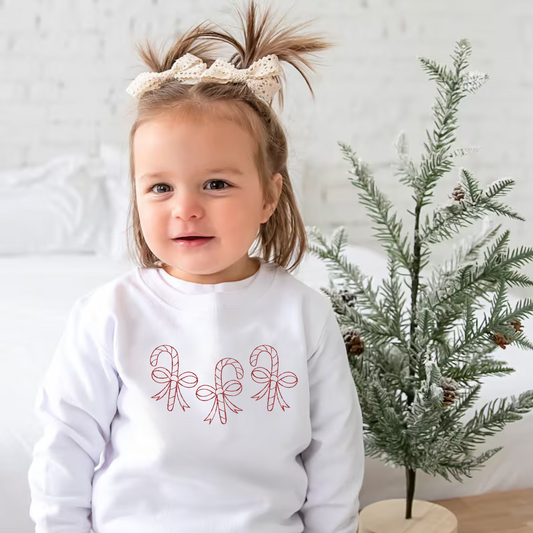 toddler girl wearing a white crewneck sweatshirt with 3 outlined candy canes wrapped in bows embroidered across the chest in red thread.