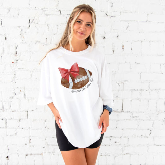 woman wearing a white comfort colors t-shirt with a custom watercolor football and red bow print with custom script text along the curve reading We Are the Colonels!