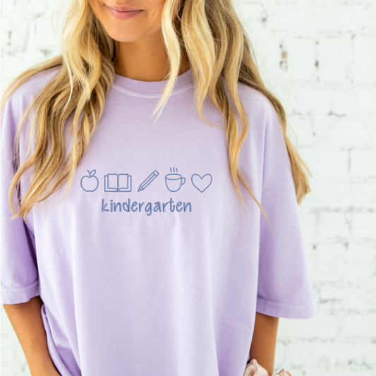 young woman wearing a lilac comfort colros t-shirt with embroidered teacher icons in periwinkle thread across the chest and custom text underneith