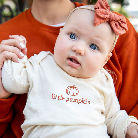 baby girl wearing a natural long sleeve bodysuit with a custom little pumpkin embroidered design