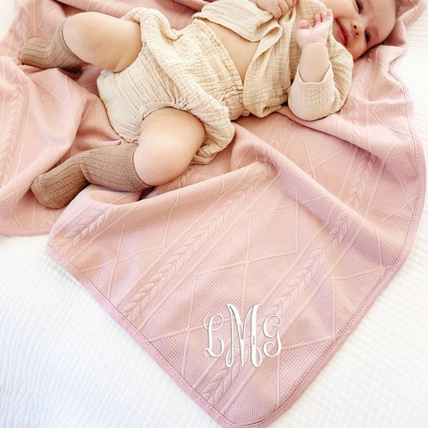 baby girl laying on a rose pink knitted blanket with a personalized monogram embroidered on the corner