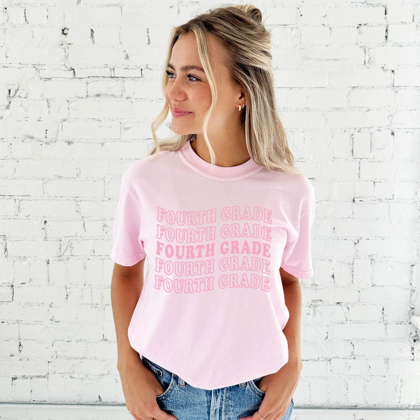woman wearing a small blossom comfort colors tee with a wavy fourth grade pink print