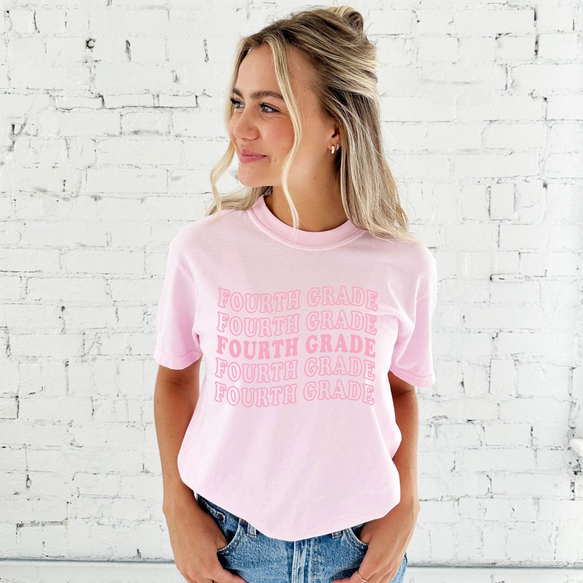 woman wearing a small blossom comfort colors tee with a wavy fourth grade pink print