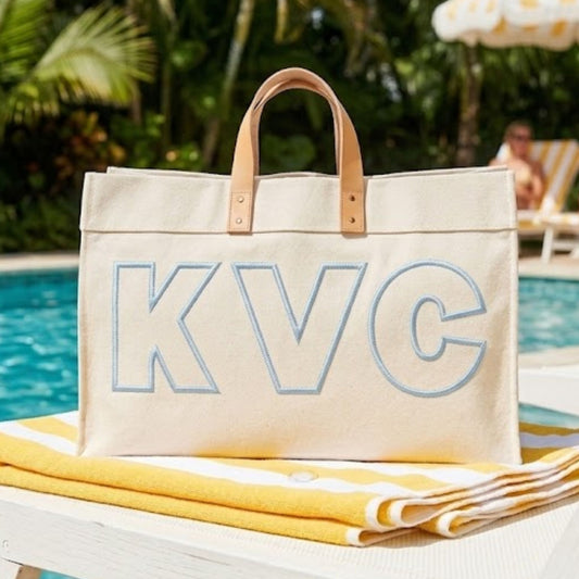 Beige tote bag with 'KVC' embroidery by a poolside