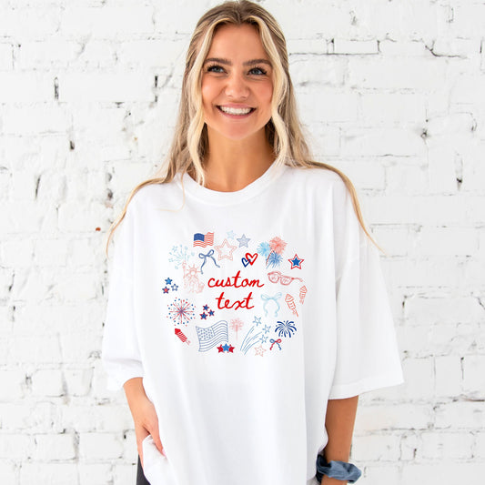 Woman wearing an oversized white custom comfort colors t-shirt featuring fun, playful patriotic doodles print with a hand-drawn aesthetic. Design features a custom text option in the center of the red, white, and blue 4th of July doodles!