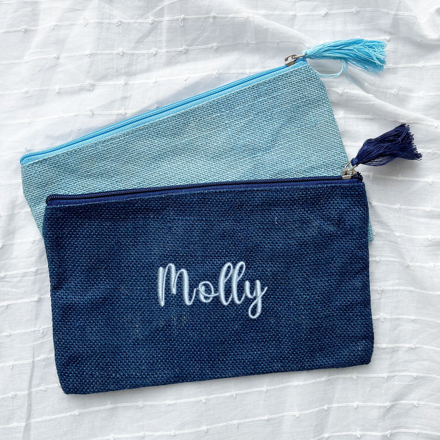 palace blue and navy zippered pouches with custom name embroidery in a cursive font and powder blue thread.