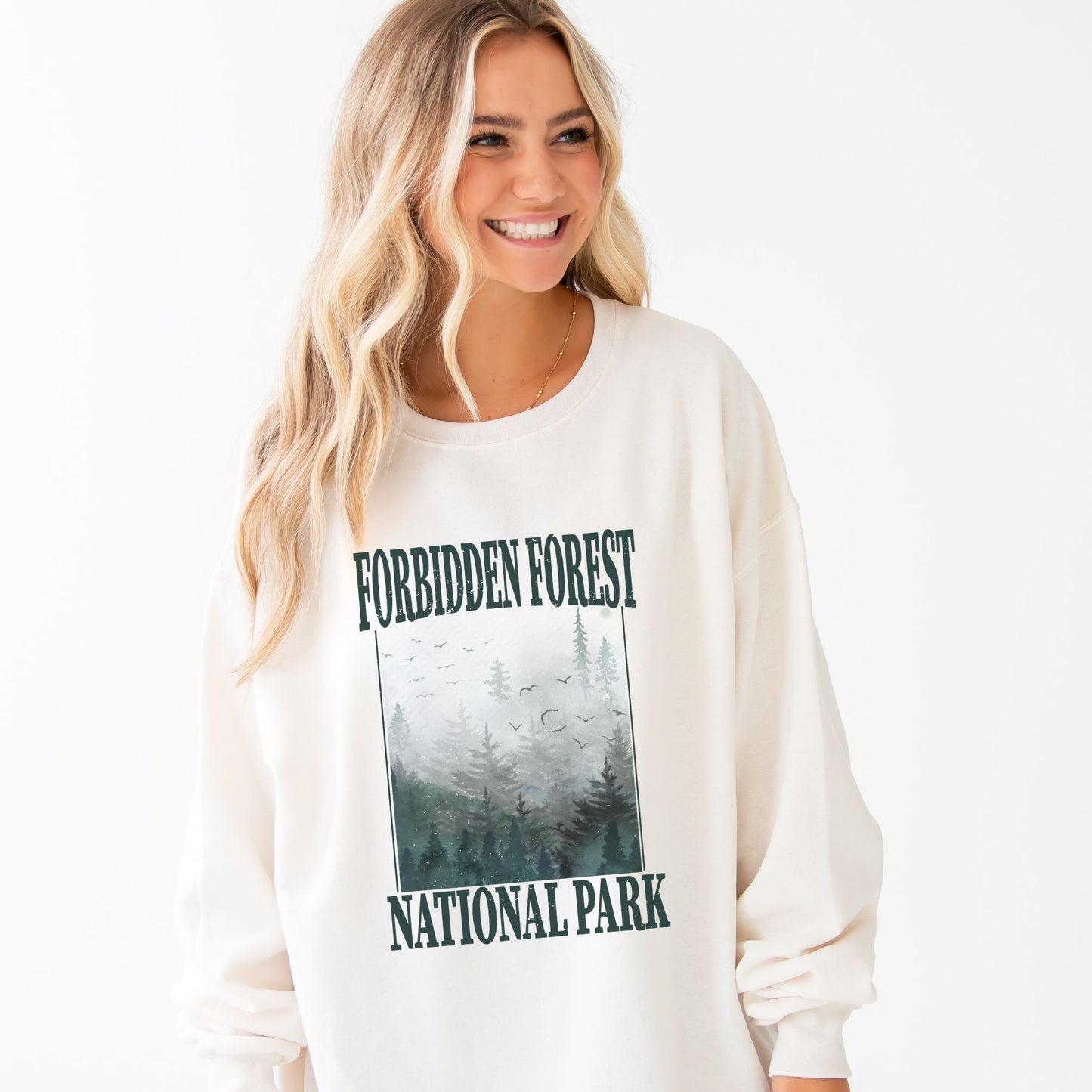 girl wearing an oversized sweet cream crewneck sweatshirt with a distressed forbidden forest national park print