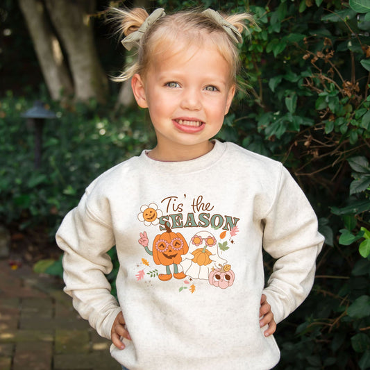 little girl wearing a heather oatmeal crewneck sweatshirt with a cute halloween print reading tis' the season with a cute ghost, pumpkin, and fall florals and leaves