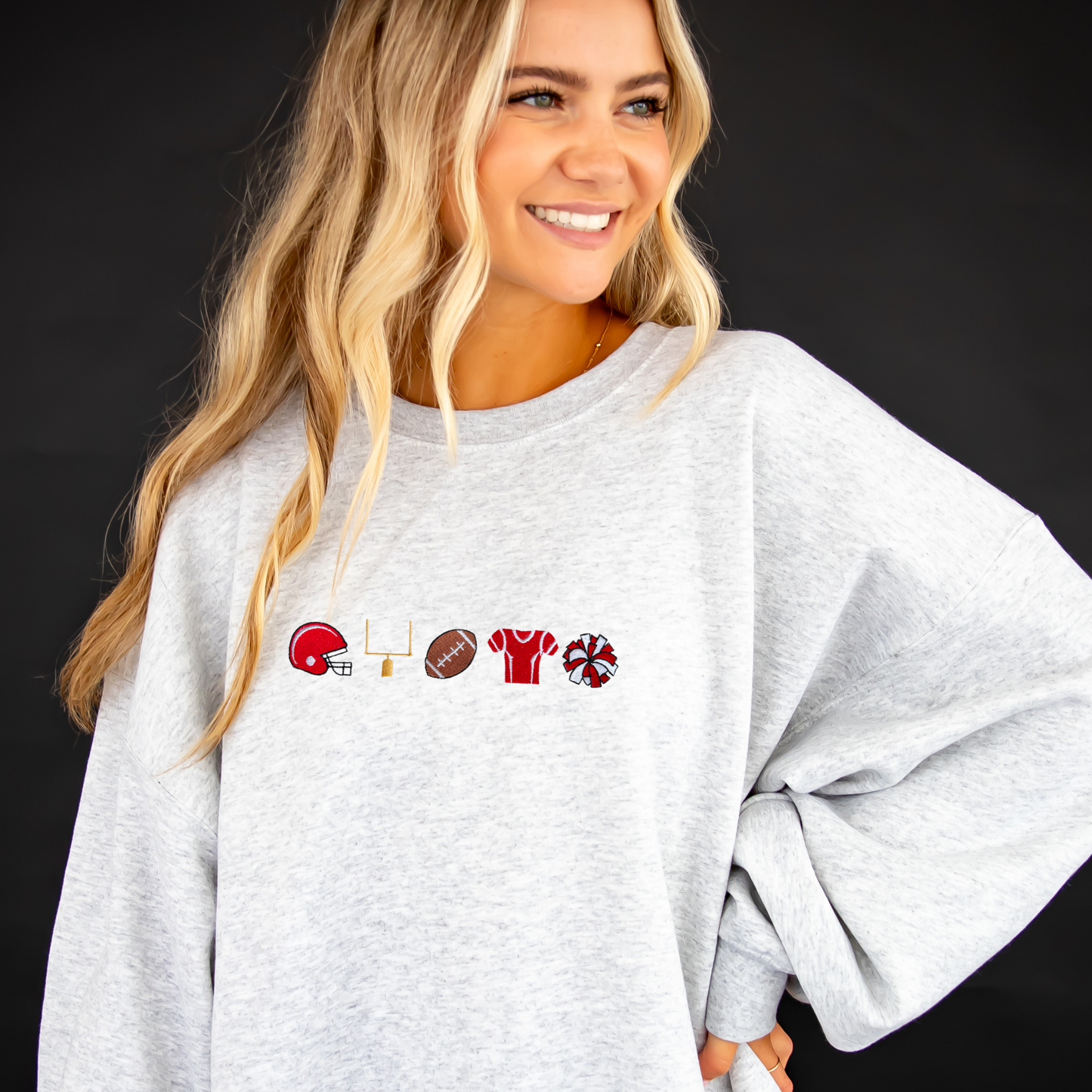 young woman wearing an ash crewneck sweatshirt with embroidered football icons in red thread