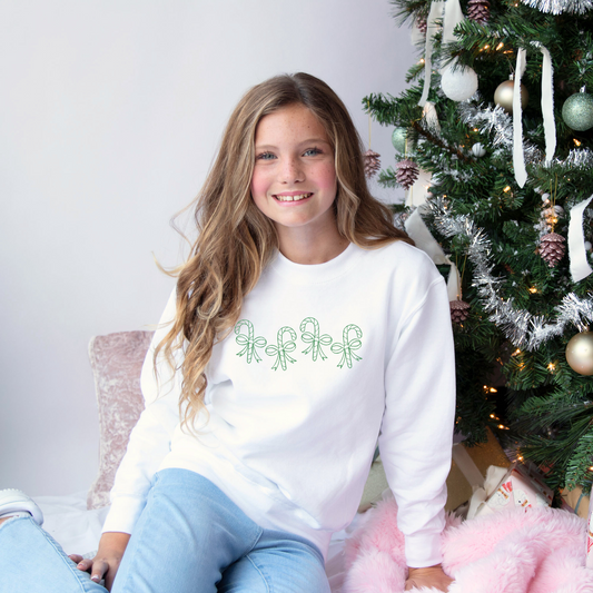 young girl wearing a white crewneck sweatshirt with stitched candy canes wrapped in bows across the chest in green thread