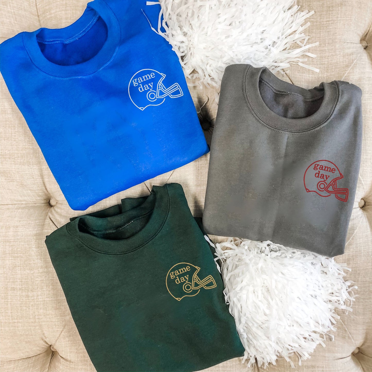 flat lay of three crew neck sweatshirts in royal blue, charcoal, and forest  green. On the left chest ifs embroidered football helmet outline with game day in inside.