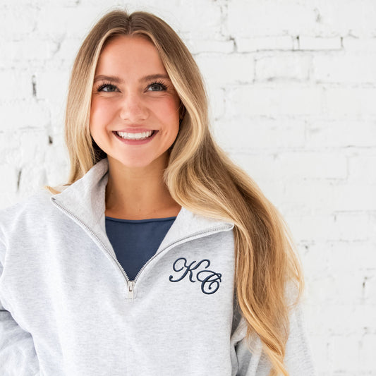 Woman wearing a gray zip-up hoodie with initials 'KC' embroidered in an Edwardian script on the left chest in navy thread