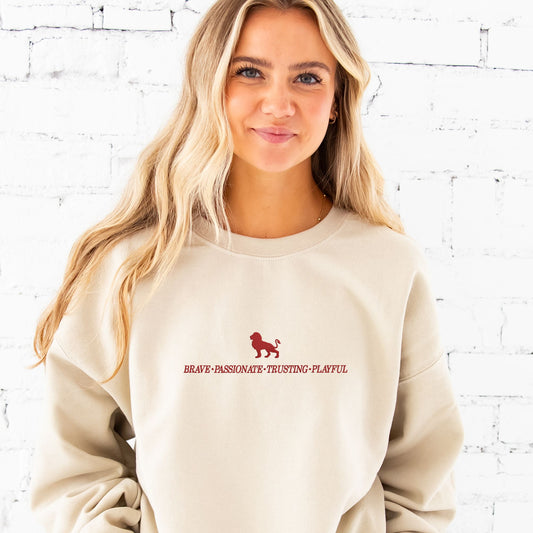 Woman wearing our Sand crewneck sweatshirt with a custom Gryffindor embroidered design featuring these keywords: brave passionate, trusting, and playful along with a lion.