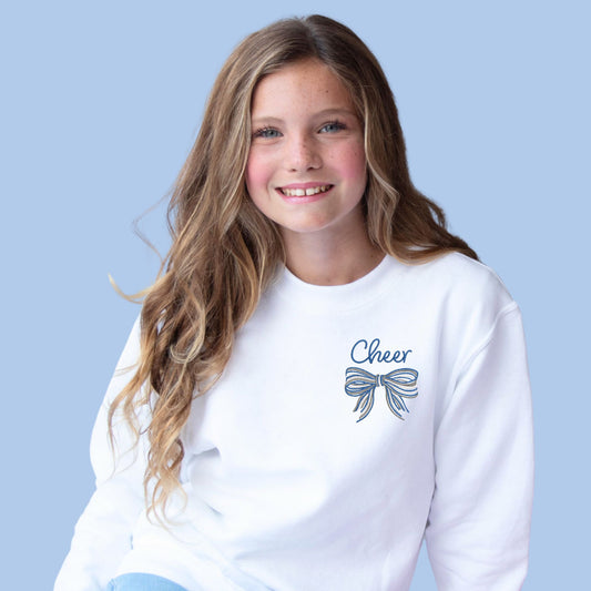 young girl wearing a white crewneck sweatshirt with embroidered cheer and striped bow in the chest chest in white, grey, and blue threads