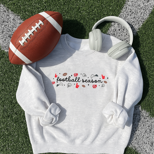 White sweatshirt with 'football season' text, football, and headphones on grass