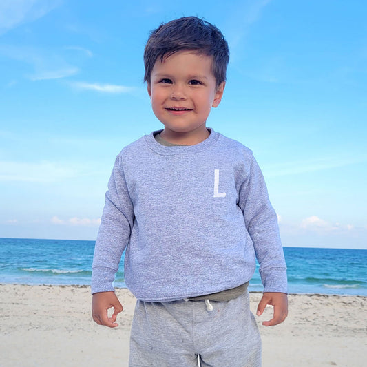 little boy on a beach wearing a gray crewneck with single intial embroidered design