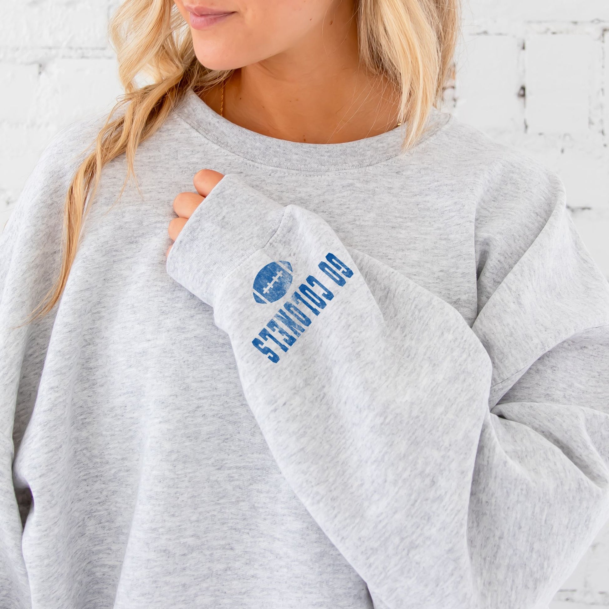 girl wearing an ash grey sweatshirt with a distressed go colonels football print on the cuff
