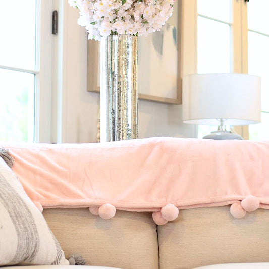 pink pom pom blanket draped over the edge of a couch