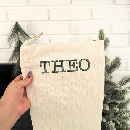 natural and silver striped stocking with custom name embroidered in Typewriter font and ivy thread hanging at a fireplace
