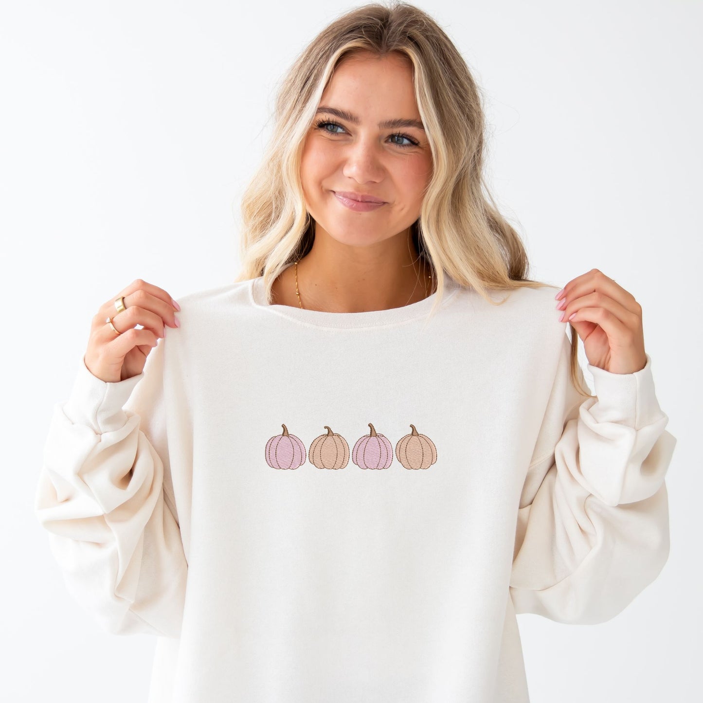 young woman wearing a sweet cream crewneck sweatshirt with embroidered 4 pumpkins in a row in alternating pink and orange threads across the chest