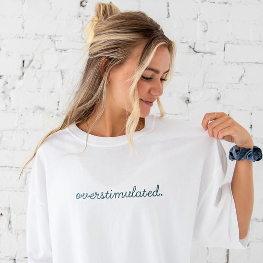 woman wearing a white comfort colors t-shirt with custom overstimulated embroidered design on the center chest in french blue thread