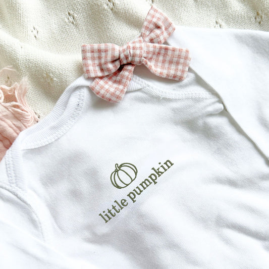 baby girl wearing a natural long sleeve bodysuit with a custom little pumpkin embroidered design