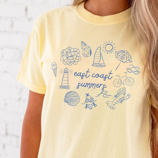 Close up of a woman wearing a banana comfort colors shirt with a custom design featuring a flower, shell, sailboat, sun, umbrella, lighthouse, clam, swimsuit, waves, lobster, bicycle, sunglasses, and east coast summer printed at the center in a script font.