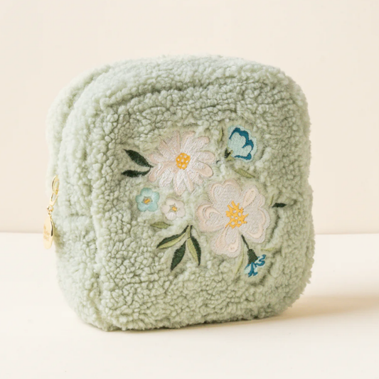 Green sherpa pouch with floral embroidery on a beige background