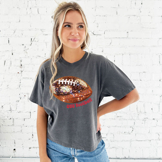 young woman wearing a cropped pepper comfort colors t-shirt with large glitter football design across the chest and OSU football curved under the football in red ink