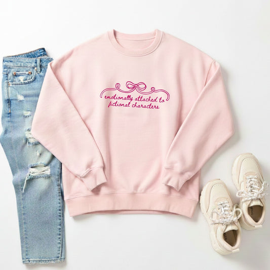 flat lay of a blush crewneck with 'emotionally attached to fictional characters' bow design printed across the chest in dark pink ink