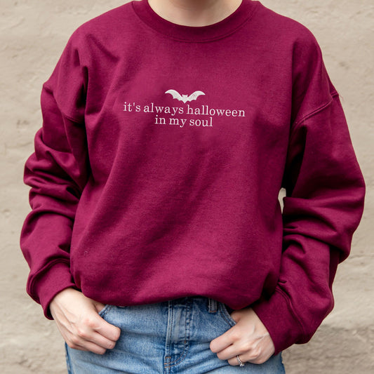 close up of a maroon crewneck sweatshirt with embroidered its always halloween in my soul and bat design across the chest in white thread