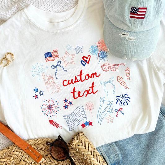 Straw tote bag, distressed denim baseball hat with mini USA flag embroidery, jeans, and a white custom comfort colors t-shirt featuring fun, playful patriotic doodles print with a hand-drawn aesthetic. Design features a custom text option in the center of the red, white, and blue 4th of July doodles!