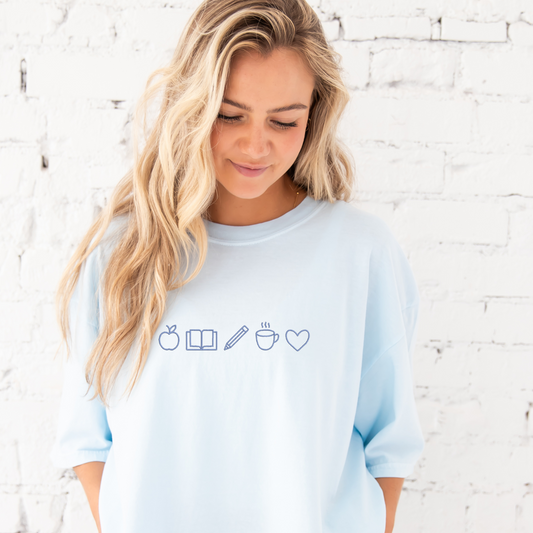 young woman wearing chambray tee with embroidered teacher icons in periwinkle thread across the chest