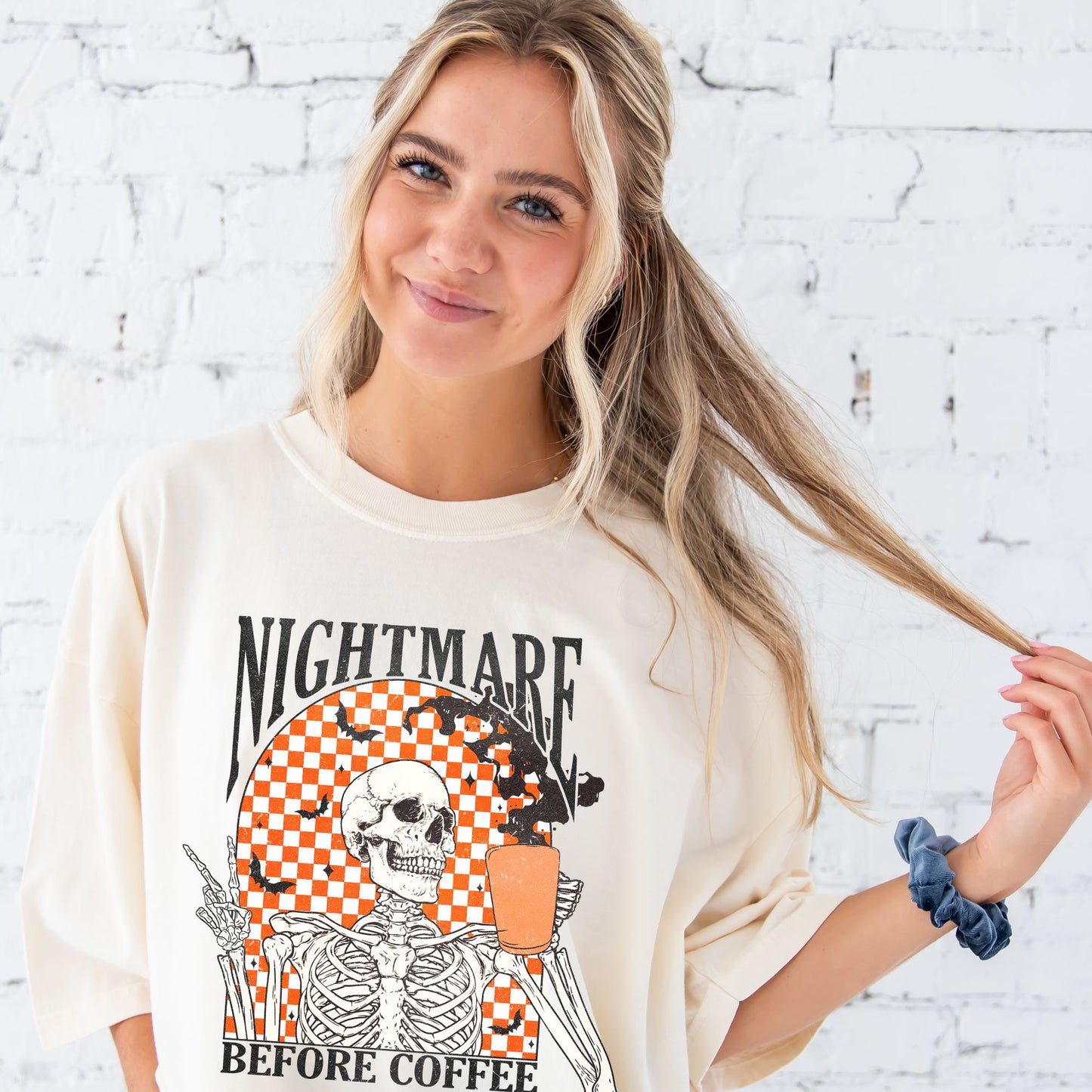 girl wearing an ivory comfort colors t-shirt with a nightmare before coffee skeleton/bat print with a checkered background