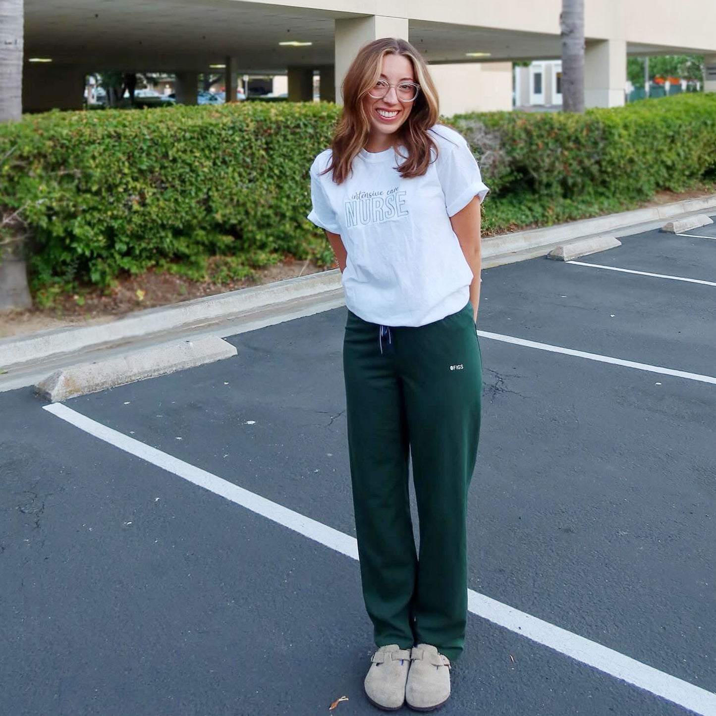 nurse wearing green figs scrub pants and a white comfort colors t-shirt with a custom intensive care nurse embroidered design in gray and eucalyptus