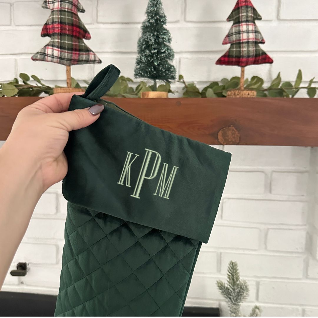 close up of a dark green quilted stocking with embroidered monogram in white thread.