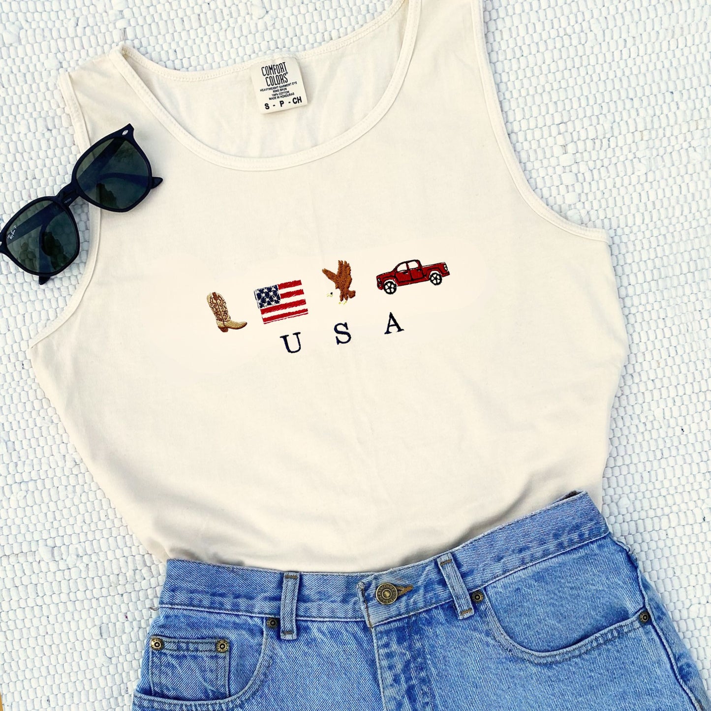 ivory comfort colors tank top with custom usa icon embroidered design on the center chest featuring a cowboy boot, american flag, bald eagle, and a pickup truck