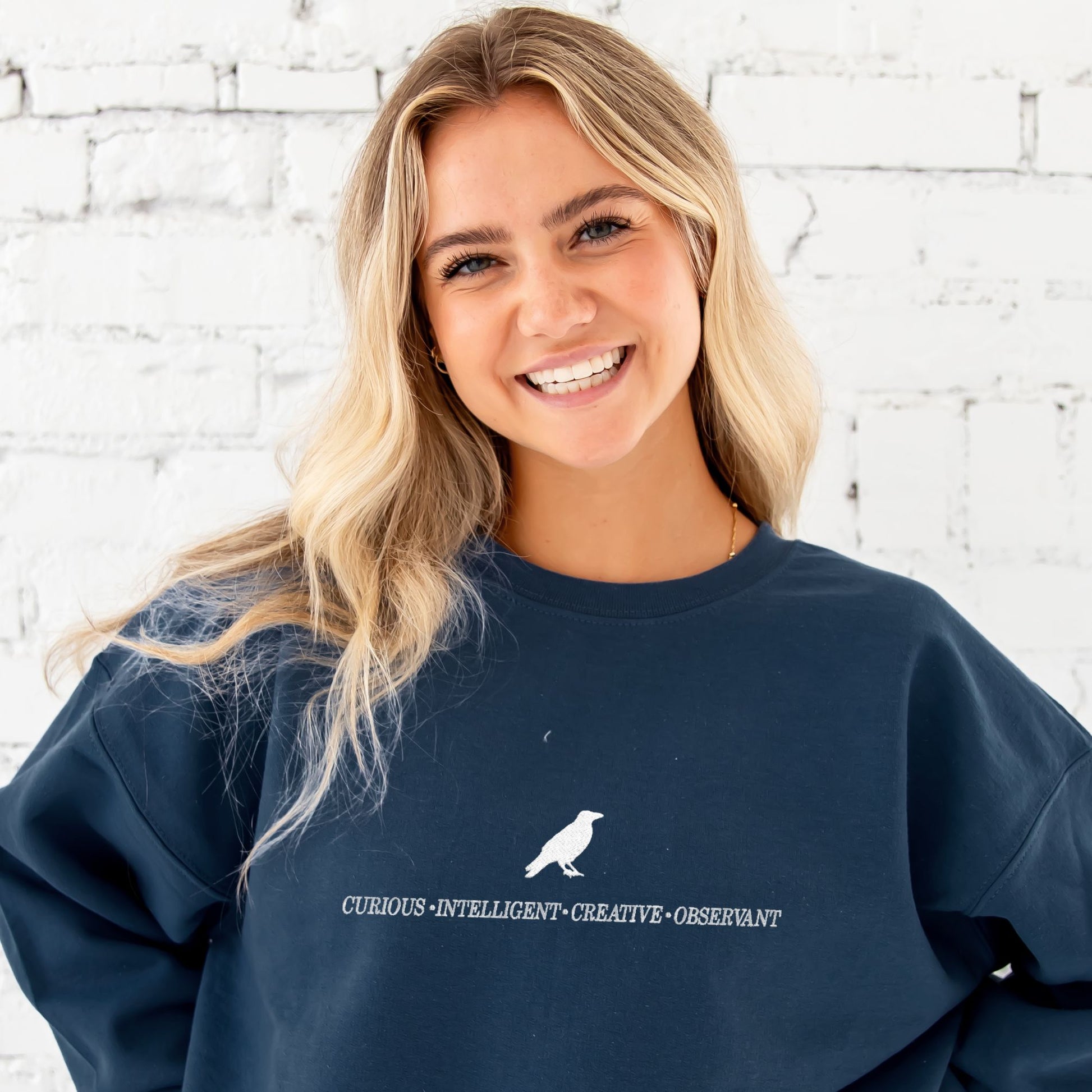 girl wearing navy crewneck sweatshirt with a custom ravenclaw embroidered design featuring a raven and these characteristics: curious, intelligent, creative, observant