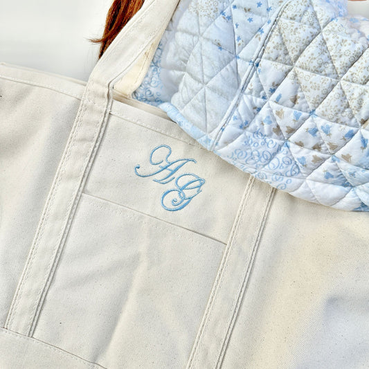 close up of edwardian script monogram embroidery in powder blue thread on a natural canvas boat tote bag looped over someones shoulder