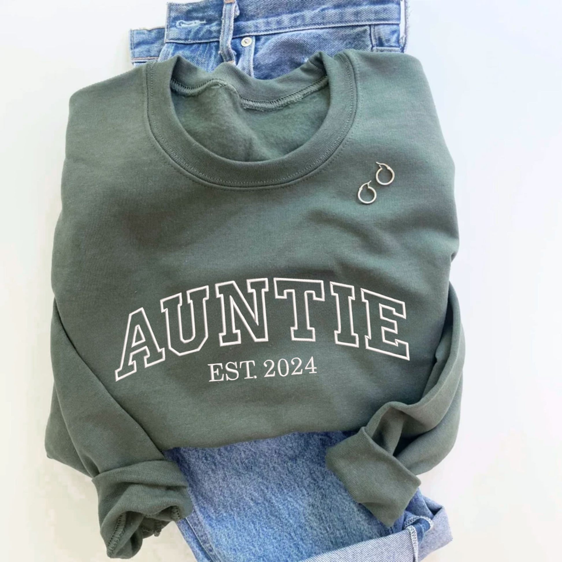flay lay image of an indigo crewneck sweatshirt with embroidered AUNTIE in all caps athletic block font and EST 2024 below in white thread.
