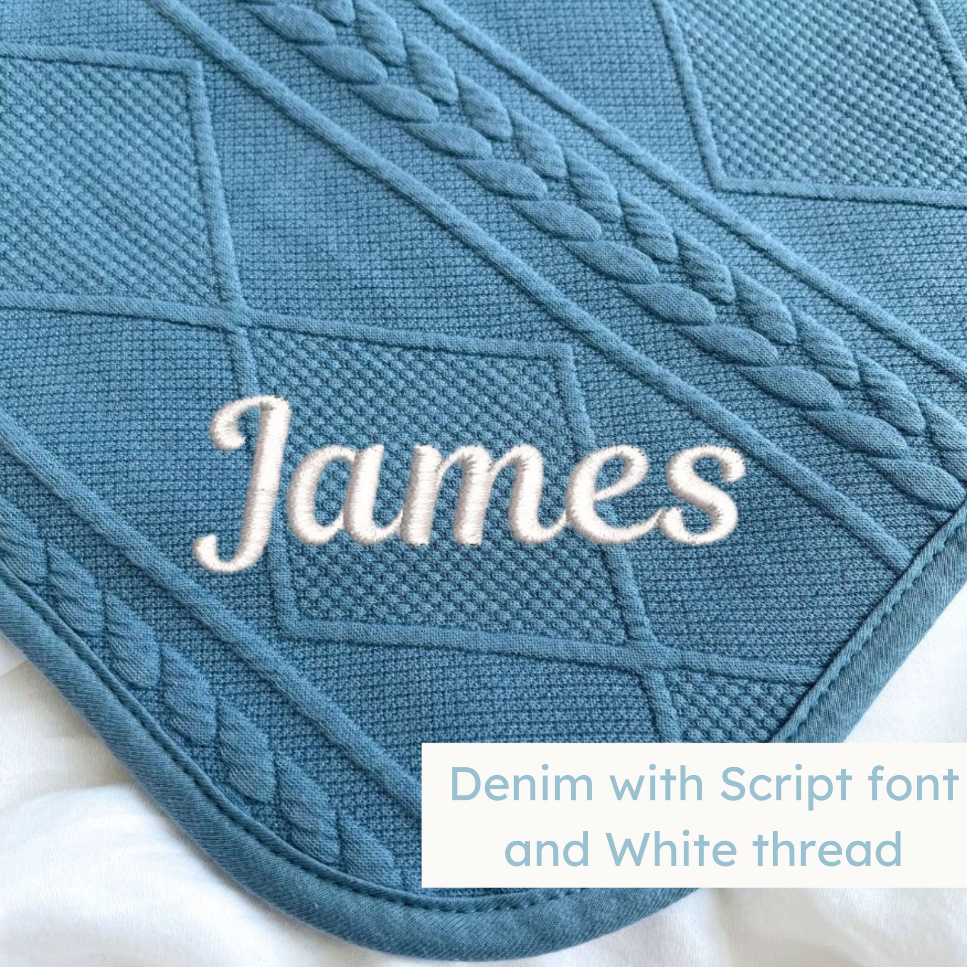 A denim blue knitted blanket with a personalized name embroidered on the corner