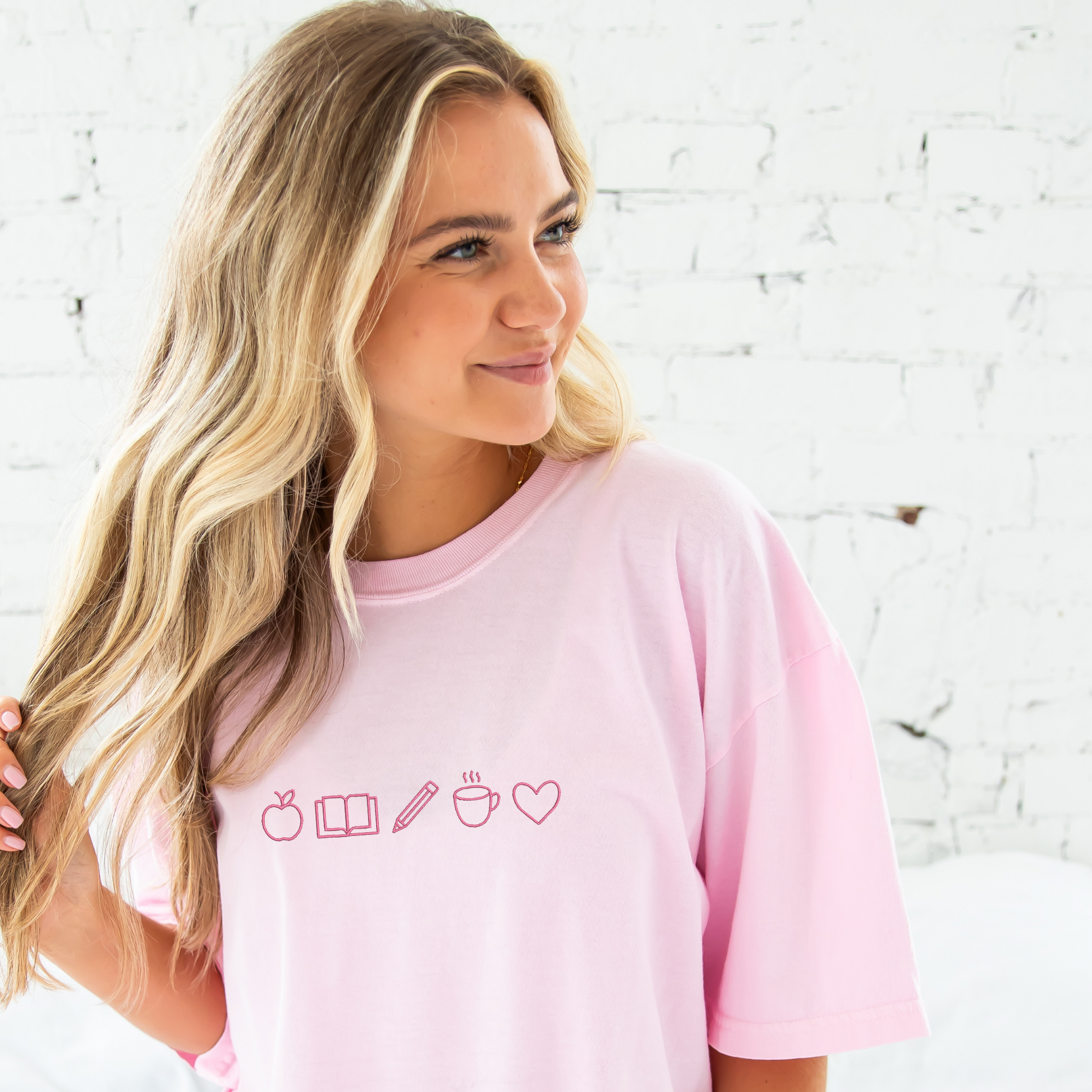 young woman wearing a blossom tee with embroidered teacher icons in pink thread across the chest