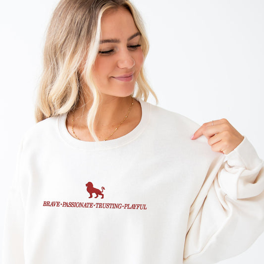 Woman wearing our Sweet Cream crewneck sweatshirt with a custom Gryffindor embroidered design featuring these keywords: brave passionate, trusting, and playful along with a lion.