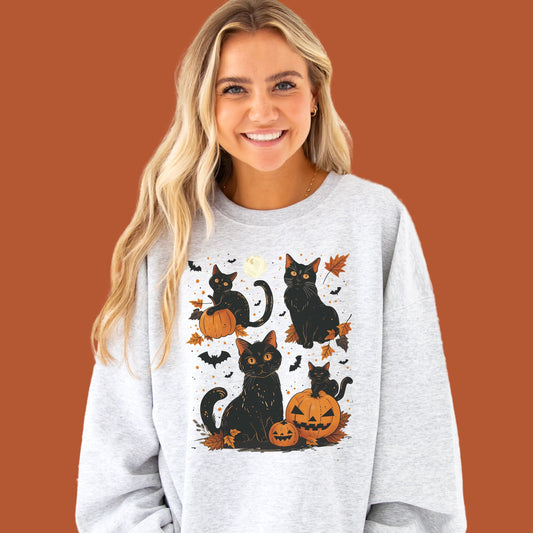 young woman wearing an ash crewneck sweatshirt with a vintage inspired black cat, jack-o-lantern, moon, leaves, and bat printed design