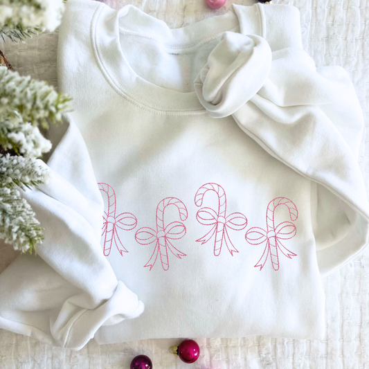 Christmas styled flat lay of a youth white crewneck sweatshirt with stitched candy canes wrapped in bows across the chest in pink thread