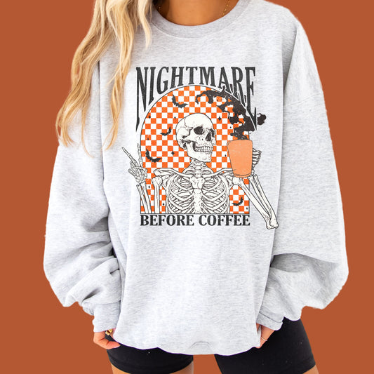 girl wearing biker shorts and an oversized ash crewneck sweatshirt with a funny, vintage, distressed skeleton drinking coffee with the text nightmare before coffee print