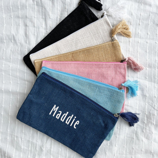 black, white, natural jute, light pink, palace blue, and navy zippered pouches with custom name embroidery in white thread and handicraft font