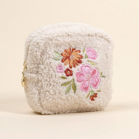 Fluffy white pouch with floral embroidery on a beige background