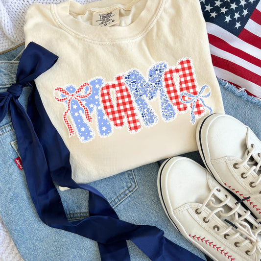 An outfit flat lay featuring the following: blue jeans, white sneakers with red stitching details, navy blue ribbon bow, USA flag, and an ivory comfort colors t-shirt with coquette bow lace mama floral and gingham print on the center chest